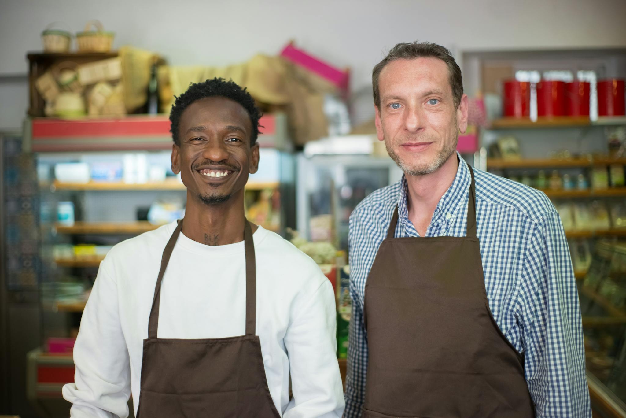 Two happy store owners smiling while wearing aprons in a local grocery store.