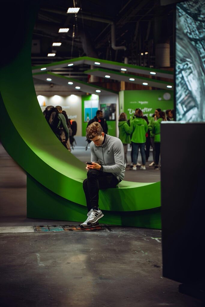 Young man sitting on a green structure using phone at indoor event